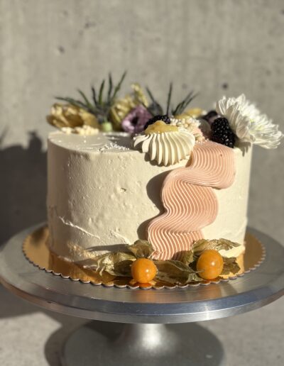 Buttercream cake decorated with dried flowers, orange slices and a pink sugar accent