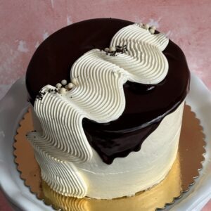 Blueberry cardamom cake with glossy dark glaze and white buttercream piping
