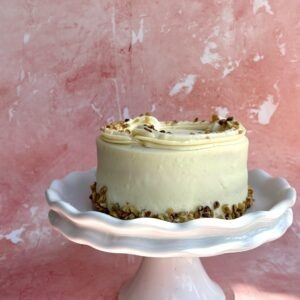 Carrot cake with cream cheese frosting and chopped nuts on a white cake stand