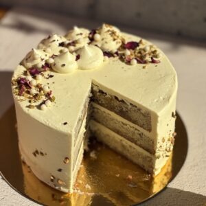 Persian love cake with a slice removed showing the layers, topped with pistachios and rose petals