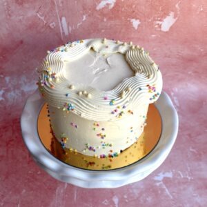 Vanilla sprinkle cake with white buttercream and rainbow sprinkles on a white cake stand