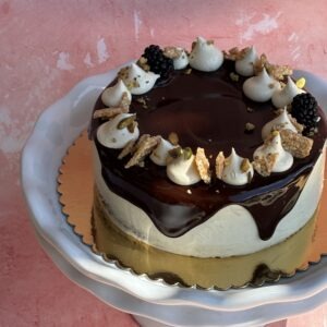 Gluten-free chocolate tahini cake with glossy chocolate ganache and white meringue swirls on a gold cake board