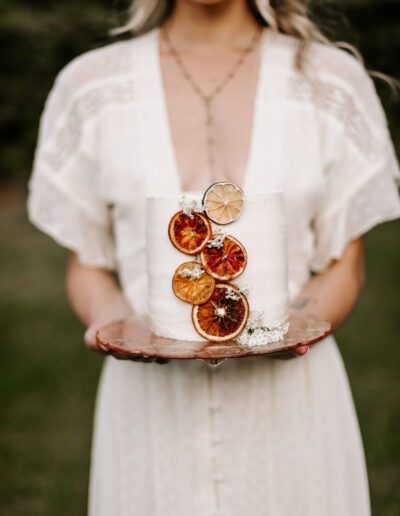 Woman in a white dress holding a wedding cake decorated with dried citrus slices