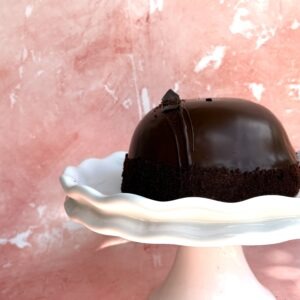 Gluten-free chocolate mousse cake with a glossy dark chocolate dome on a white cake stand, from Epiphany Cakes in Nelson, BC